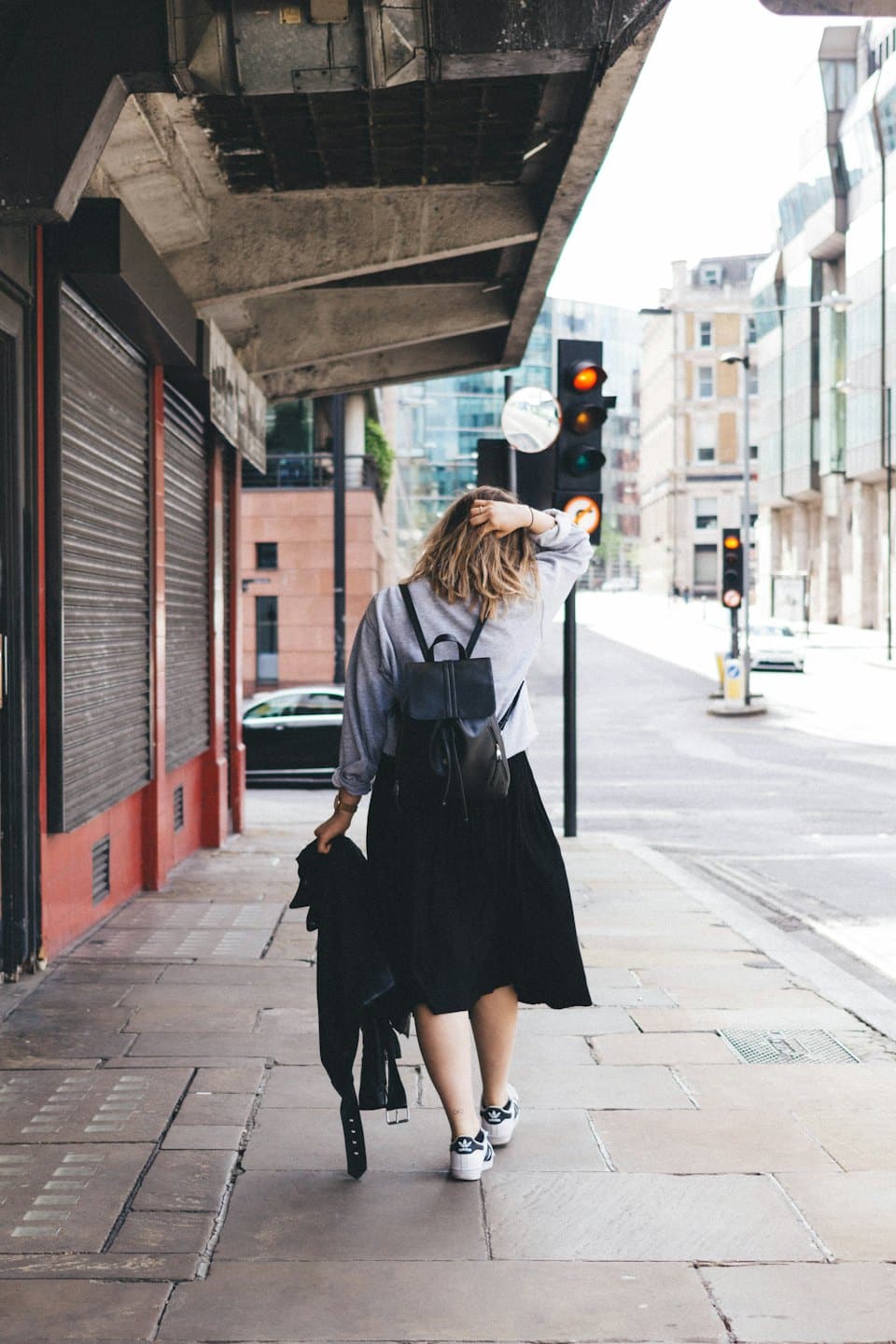 Woman walks down a sunny city sidewalk with a backpack.